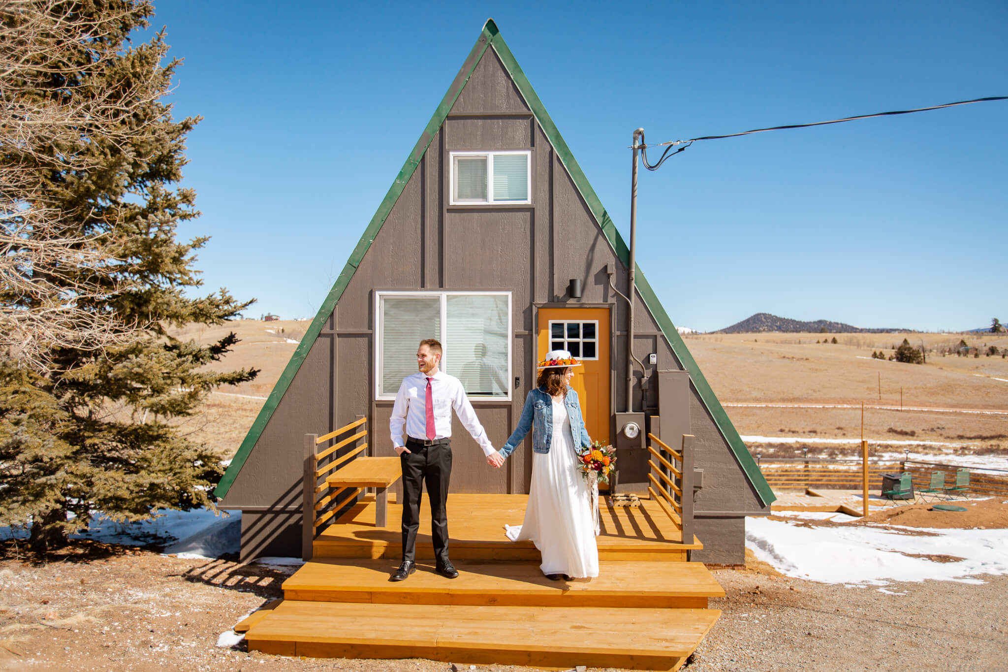 Couple holding hands and posing in front of cozy cabin.