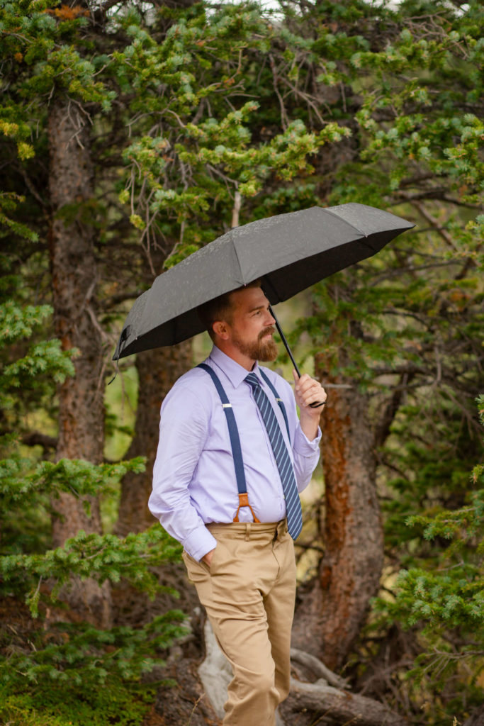 groom holding an umbrella waiting for first look