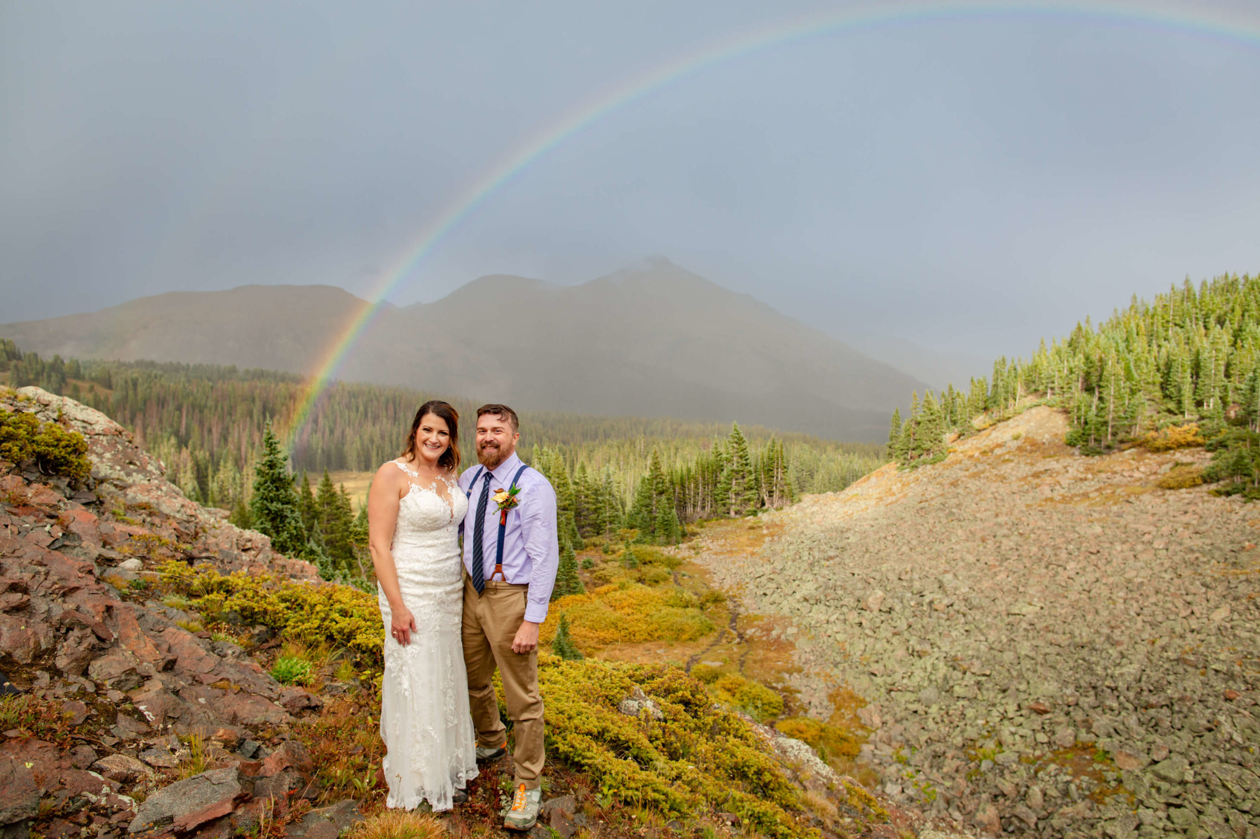 bride and groom posing in front of rainbow