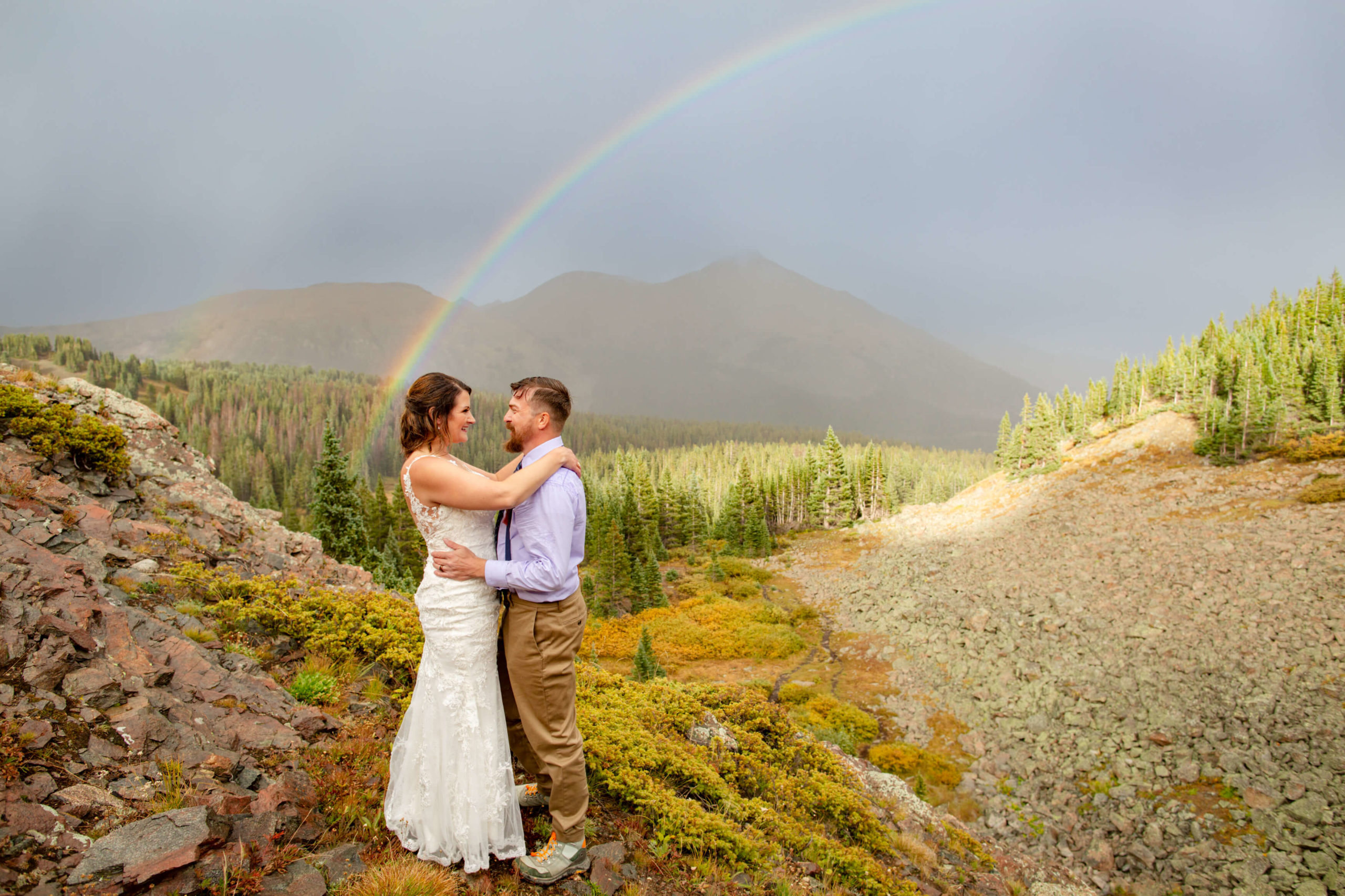 couple holding each other in front of rainbow and mountains