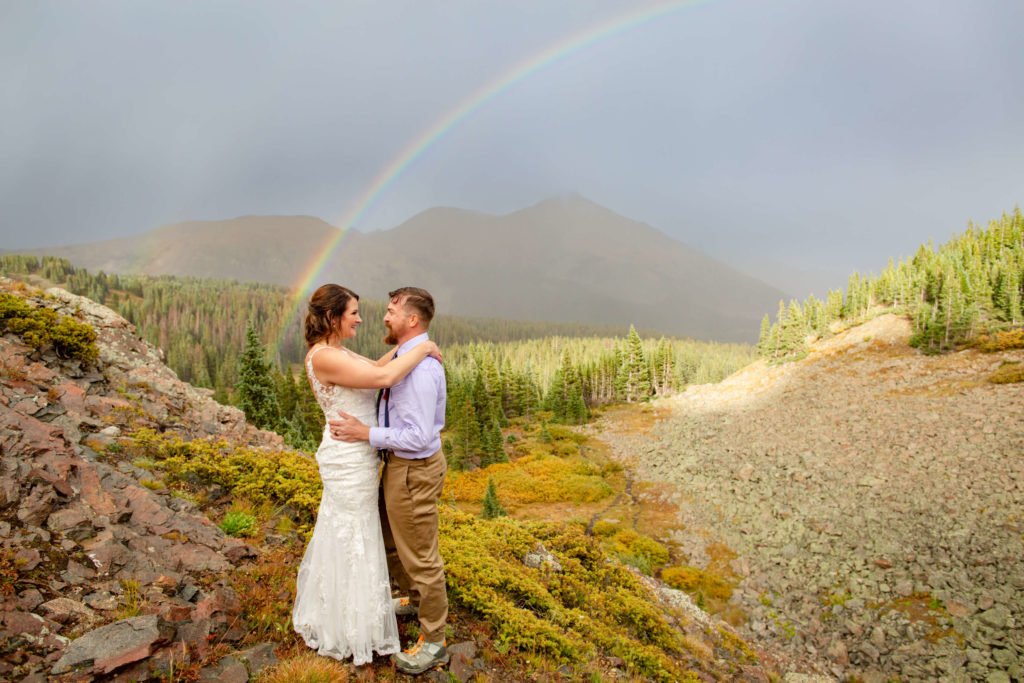 couple holding each other in front of a rainbow