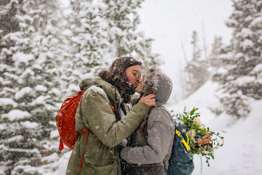 Groom kisses bride as they hike in the snow for their Rocky Mountain Elopement
