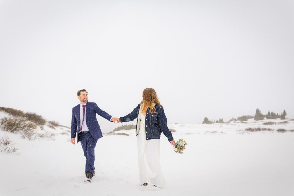 Bride and groom holding hands while walking through a winter wonderland.