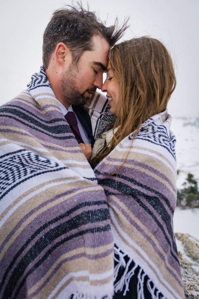 The bride and groom are wrapped in a blanket, holding each other.