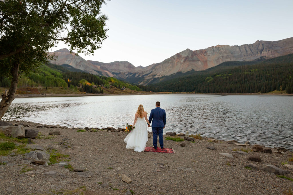 bride and groom facing the lake and Telluride mountain range while holding hands