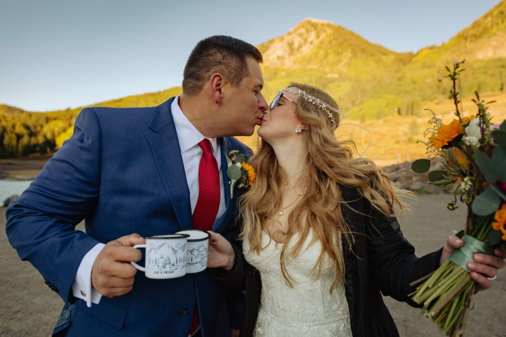 bride and groom kissing while holding their mugs with champagne