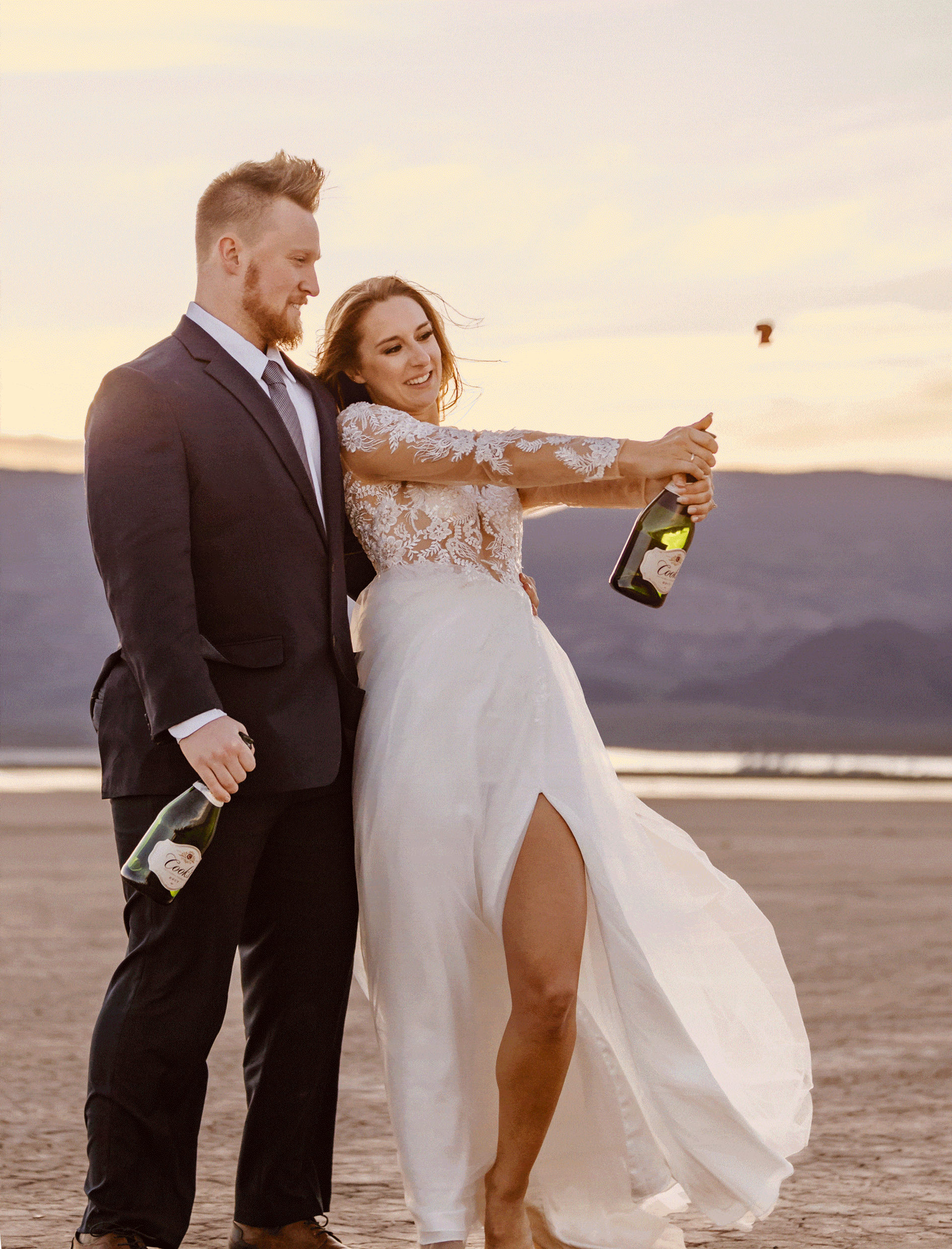 Gif of bride popping and spraying champagne while the groom stands next to her holding her hip during their elopement at a dry lake bed in Las Vegas.