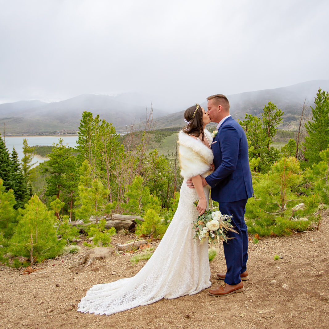 Bride and groom kiss with gloomy skies above.