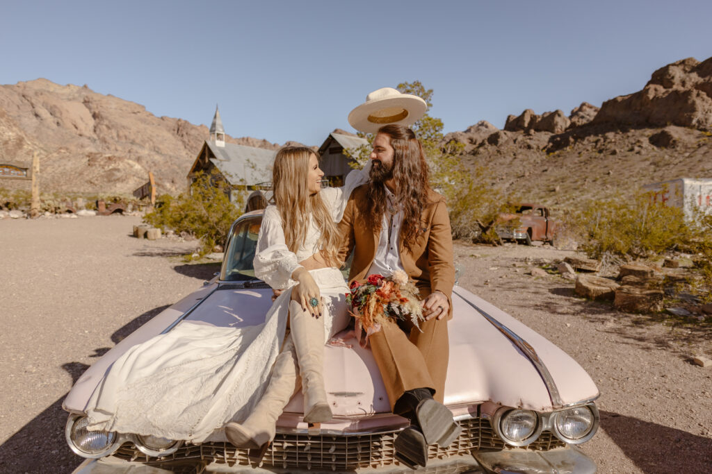 Bride puts her hat on the groom while they sit on top of a pink car during their Las Vegas elopement at Nelson's Ghost town.