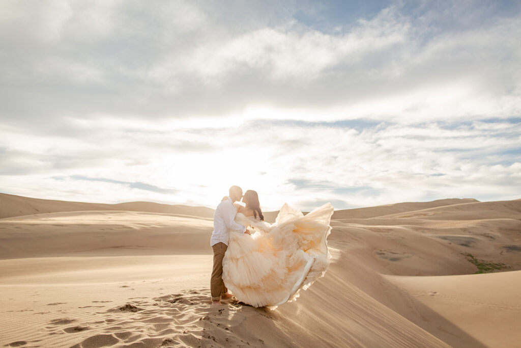 Bride and groom stand on top of a sand dune during the sunset for their elopement.