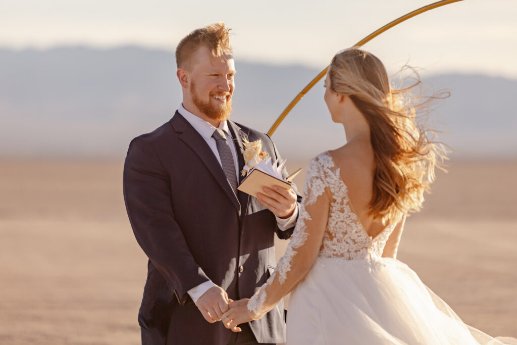 Groom smiles and looks at his bride while reciting his vows during their elopement ceremony at a dry lake bed in Las Vegas.
