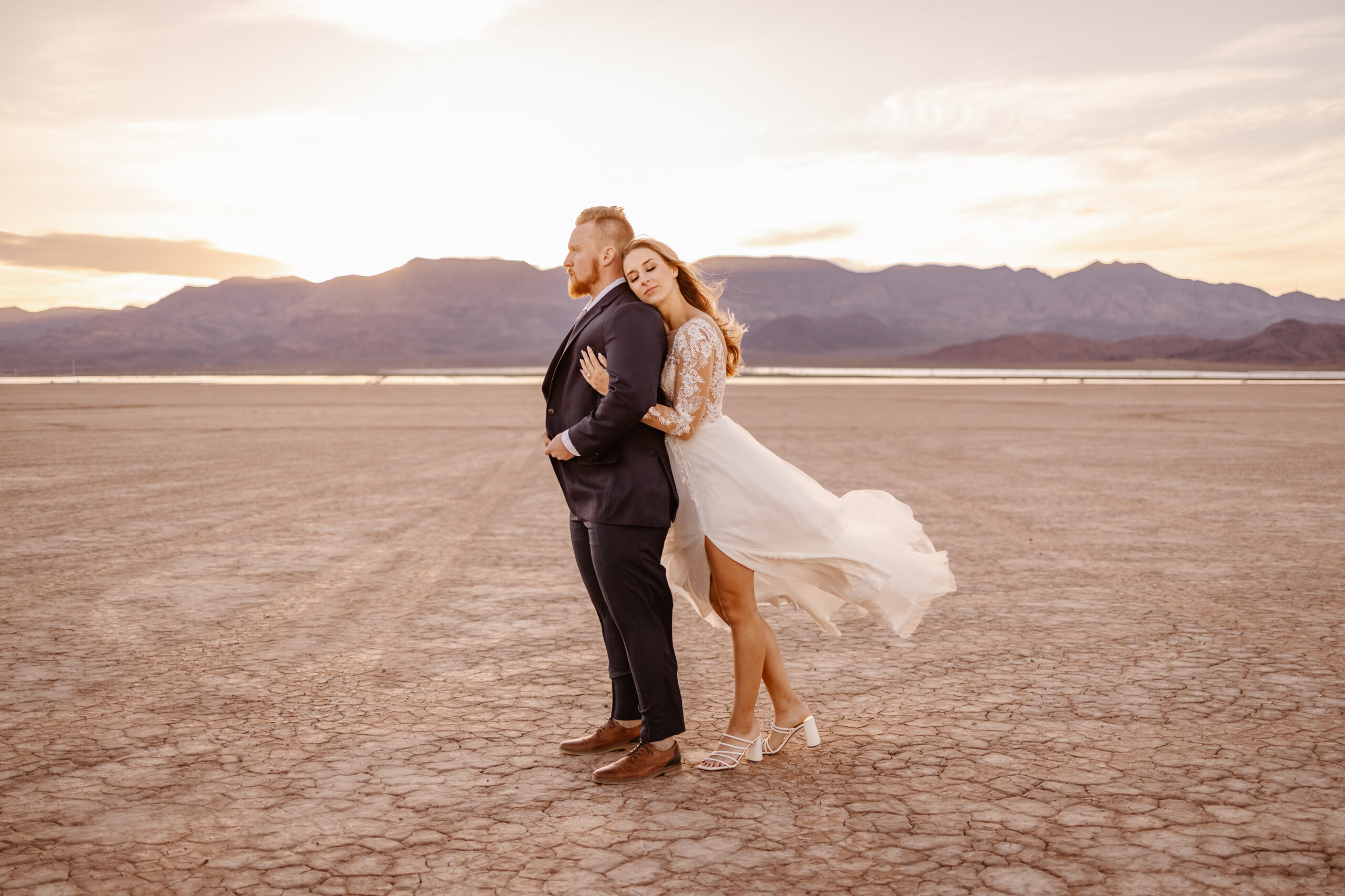 Bride hugs groom from behind at sunset during their elopement at a dry lake bed in Las Vegas