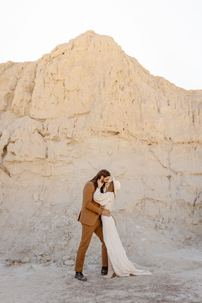 The bride and groom kiss by a white rock at Nelson's Ghost Town.