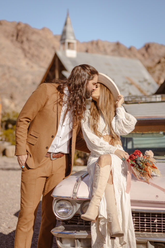 Groom and bride kiss on a pink car during their elopement at Nelson's Ghost Town.