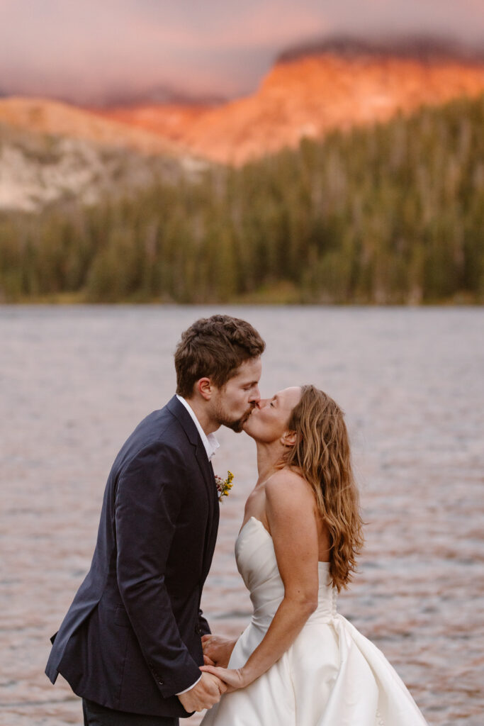 Bride and groom kiss as the mountains glow behind them from the sunrise