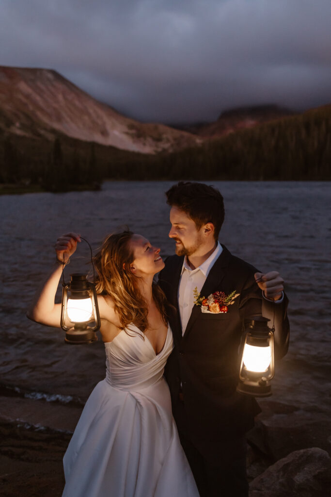 bride and groom look at each other and hold lanterns during blue hour before the sun comes up