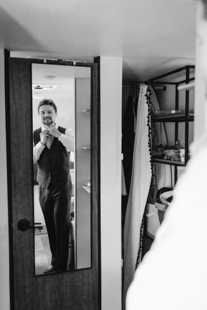 Groom adjusts tie in his trailer mirror as he gets ready for his elopement in Steamboat Springs