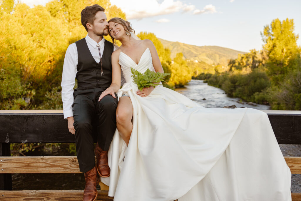 Bride and groom sit next to each other on top of a bridge in steamboat springs