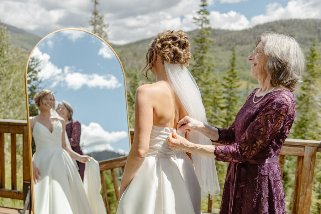 Mom helps bride button up her wedding dress on the balcony of a yurt in steamboat springs