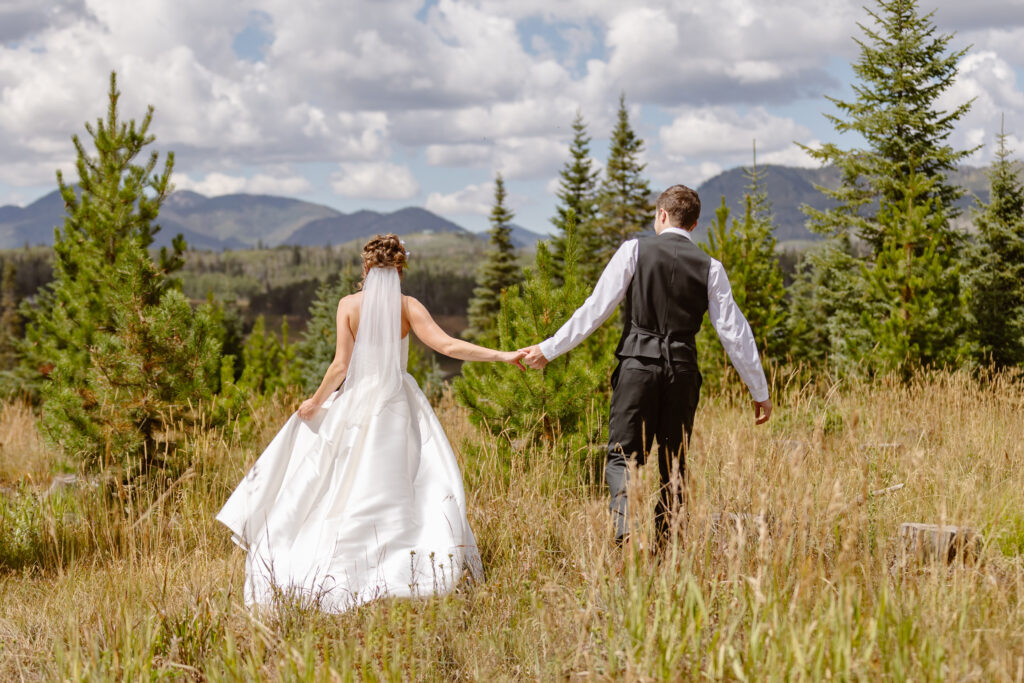 Bride and groom hold hands and run through the field towards the mountains in steamboat springs
